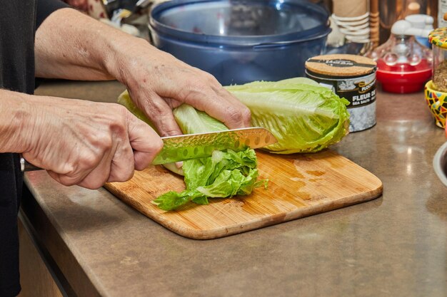 Koch schneidet Salat auf Holzbrett in der heimischen Küche