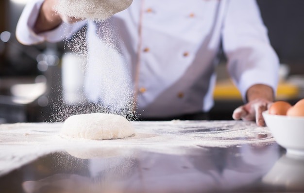 Koch streut Mehl über frischen Pizzateig auf dem Küchentisch