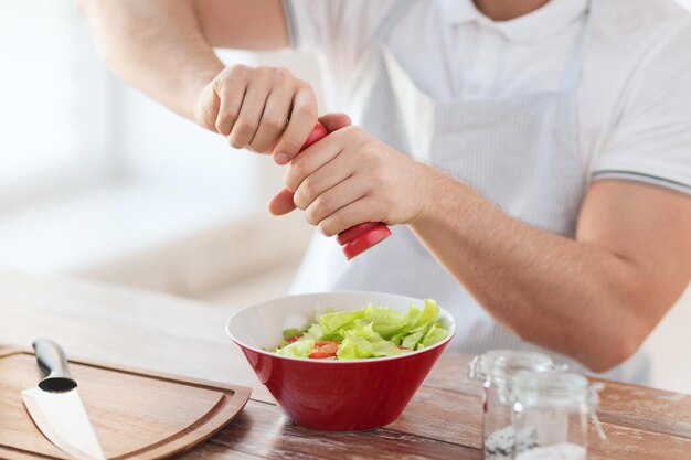 Koch- und Heimkonzept - Nahaufnahme männlicher Hände, die Salat in einer Schüssel würzen