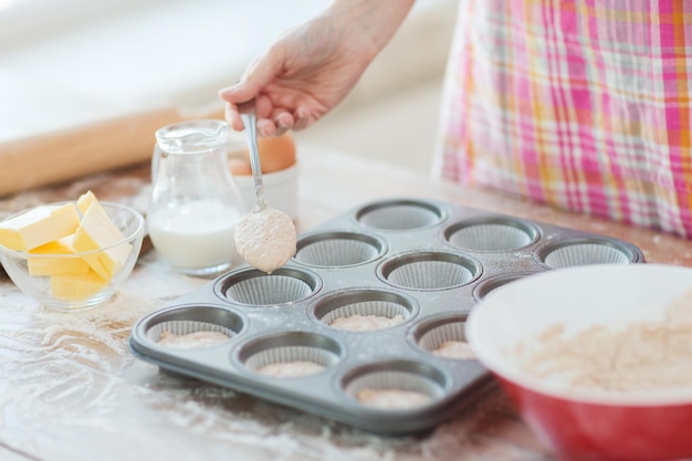 Koch- und Heimkonzept - Nahaufnahme von Hand, die Muffinsformen mit Teig füllt