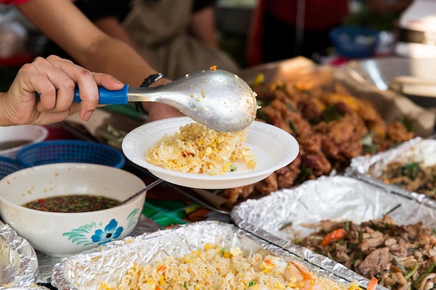 Kochen, asiatische Küche, Verkauf und Lebensmittelkonzept - Nahaufnahme von Händen mit Teller, Löffel und Wok auf dem Straßenmarkt