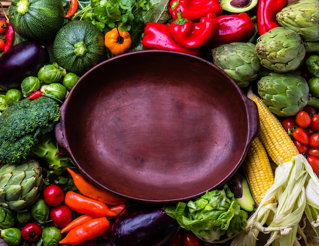 Kochen des Herbsternte-Hintergrundkonzeptes. Frisches organisches Gemüse um leeren Tongefäß