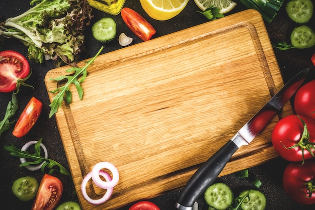 Kochen des Hintergrundes, der frischen Salatbestandteile, der italienischen Küche - Tomaten, Olivenöl, Zitrone, Gurken, Arugula, Petersilie, Zwiebeln, mit Messer und Schneidebrett