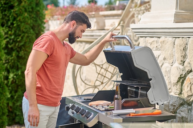 Kochen. Ein Mann in einem roten T-Shirt, der im Hinterhof gegrilltes Gemüse kocht