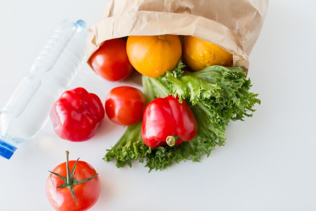 Kochen, Ernährung, vegetarisches Essen und gesundes Ernährungskonzept - Nahaufnahme einer Papiertüte mit frischem, reifem, saftigem Gemüse und einer Wasserflasche auf dem Küchentisch zu Hause