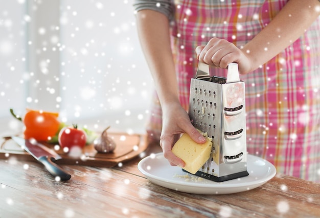 Kochen, Essen, Menschen und Wohnkonzept - Nahaufnahme weiblicher Hände mit Reibe und Gemüse, die Käse in der Küche reiben