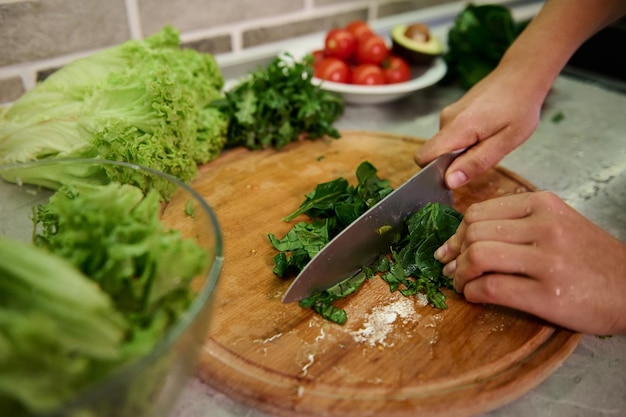 Foto kochen. essen und konzept von veganismus, vitalität und gesunder ernährung - nahaufnahme von weiblicher hand, die gemüse und spinatblätter für salat schneidet. gesunde zutaten für rohen veganen salat