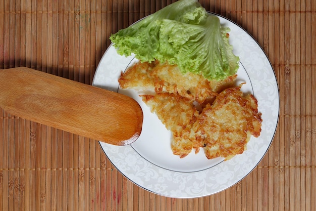 Kochen hausgemachter Kartoffelpuffer mit grünem Salat auf einem weißen Teller auf Holzhintergrund Vegetarisches Essenskonzept Nahaufnahme