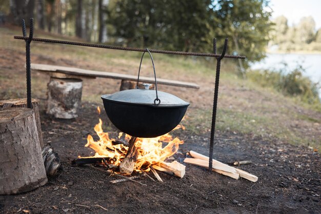 Kochen im Kessel am offenen Feuer in der Natur Bowler am Lagerfeuer im Wald Topf aus Gusseisen am Lagerfeuer auf dem Hintergrund des Flusses Platz kopieren