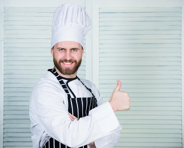 Kochen ist meine Leidenschaft Profi in der Küche kulinarische Küche Koch im Restaurant Küchenchef bereit zum Kochen selbstbewusster Mann in Schürze und Hut Daumen hochhalten glücklicher bärtiger Mann liebt Essen