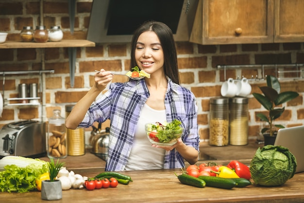 Kochen junge Frau in der Küche mit Löffel. Versucht Essen. Lächelnd.