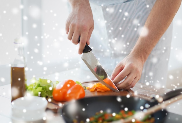 Kochen, Menschen, vegetarisches Essen und Wohnkonzept - Nahaufnahme eines Mannes, der Paprika und anderes Gemüse auf einem Schneidebrett mit einem großen Messer hackt