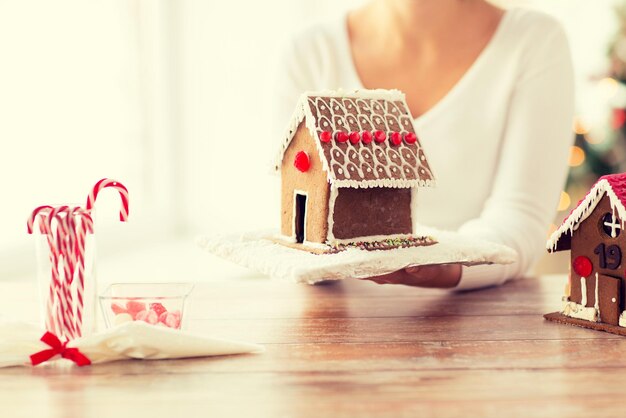 Kochen, Menschen, Weihnachten und Backkonzept - Nahaufnahme einer glücklichen Frau, die zu Hause ein Lebkuchenhaus hält und zeigt