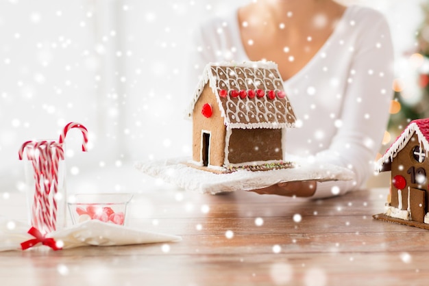 Kochen, Menschen, Weihnachten und Backkonzept - Nahaufnahme einer glücklichen Frau, die zu Hause ein Lebkuchenhaus hält und zeigt