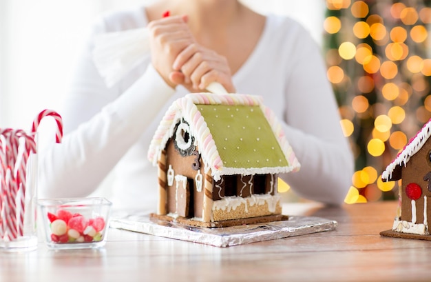 Kochen, Menschen, Weihnachten und Dekorationskonzept - glückliche Frau, die zu Hause Lebkuchenhäuser herstellt