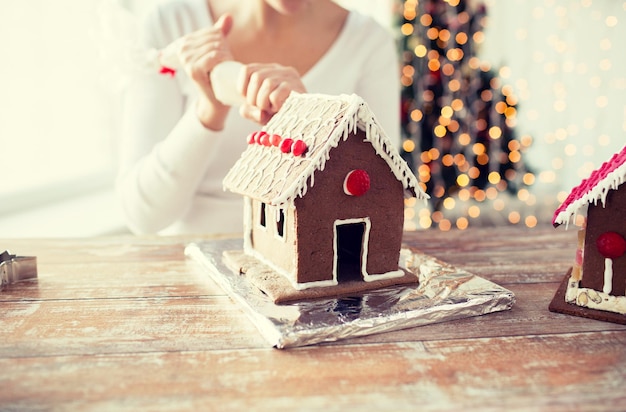 Kochen, Menschen, Weihnachten und Dekorationskonzept - Nahaufnahme einer glücklichen Frau, die zu Hause Lebkuchenhäuser herstellt