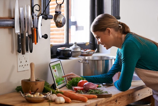 Kochen Schritt für Schritt Aufnahme einer jungen Frau, die sich ein Online-Rezept auf ihrem digitalen Tablet ansieht, während sie eine Mahlzeit zubereitet