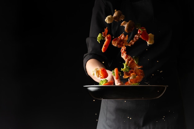 Kochen Sie die Zubereitung von Speckscheiben mit Knoblauch und Peperoni und Brokkoli in einer Pfanne, die in der Luft auf einem schwarzen Hintergrund einfriert Rezeptbuch Menü Gastronomie kulinarischer Hintergrund