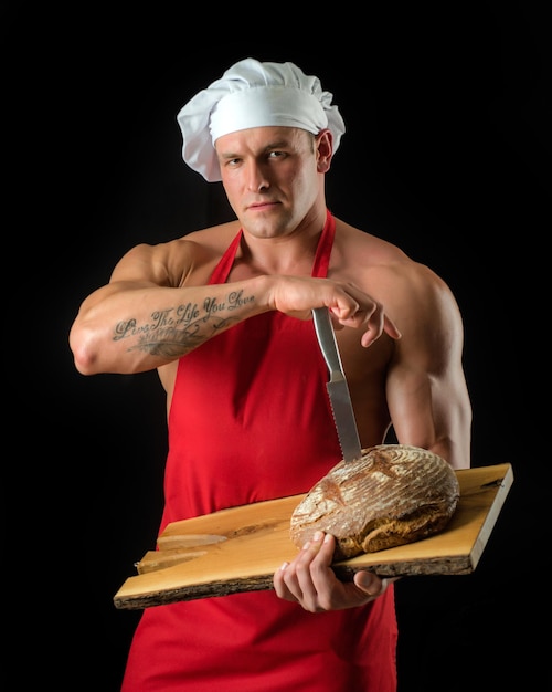 Kochen und Backen. Chefbäckermann in der Schürze. Sexy Kerl mit Brot und Messer.