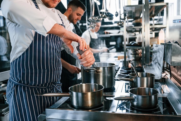 Kochen und Zutaten hinzufügen Küchenarbeiter bereiten gemeinsam das Essen zu