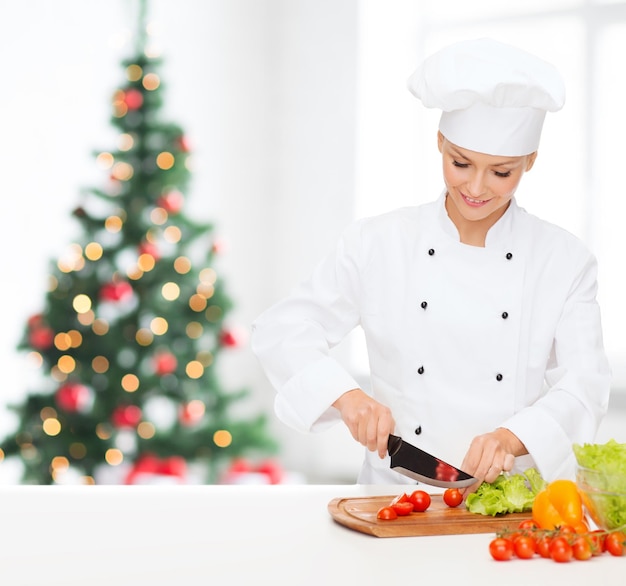 Kochen, Urlaub, Menschen und Lebensmittelkonzept - lächelnde Köchin, die Gemüse über Wohnzimmer mit Weihnachtsbaumhintergrund hackt