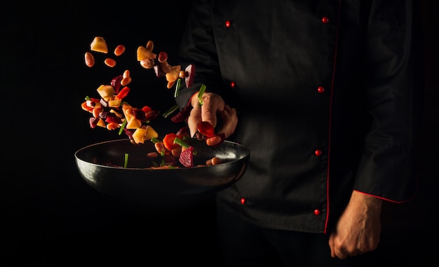 Kochen von Gemüse durch Chefhände auf dunklem Hintergrund kopieren Raum