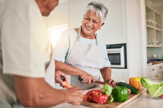 Kochen von Gemüse in der Küche und älteres Paar, das Zutaten schneidet, Essen zubereitet und bei einem romantischen Date zu Hause lächelt. Gesundheitsernährungsberater, kulinarischer und hungriger Mann, Frau oder Menschen, die sich beim Mittagessen treffen