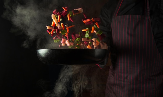 Kochen von Gemüse in einer Bratpfanne in den Händen eines Kochs für ein vegetarisches Essen Werbefläche