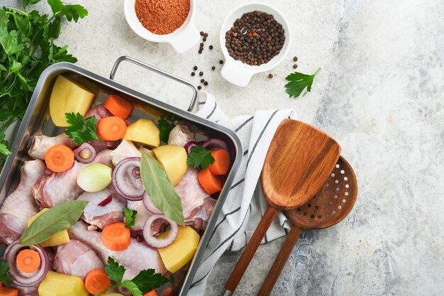 Kochen von Hühnerbouillon oder Braten in Kochpfanne oder Topf mit Gemüse, Kartoffeln, Karotten und Kräutern auf Küchenarbeitsplatte aus grauem Beton von oben Kochen, Zubereitung von Hühnerbrühe Mock up