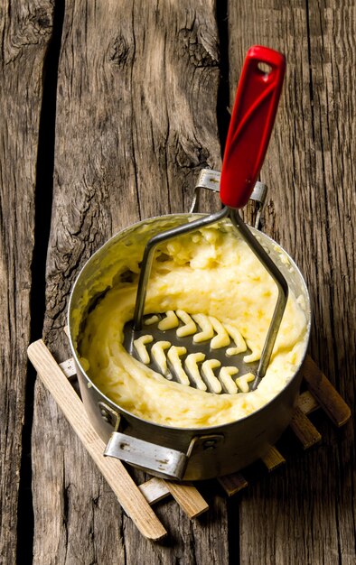 Kochen von Kartoffelpüree mit Stößel auf hölzernem Hintergrund