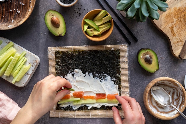 Kochen von Sushi-Rollen zu Hause mit Lachs, Avocado und Gurke Weibliche Hand, die Avocado-Sushi-Draufsicht Schritt für Schritt zubereitet