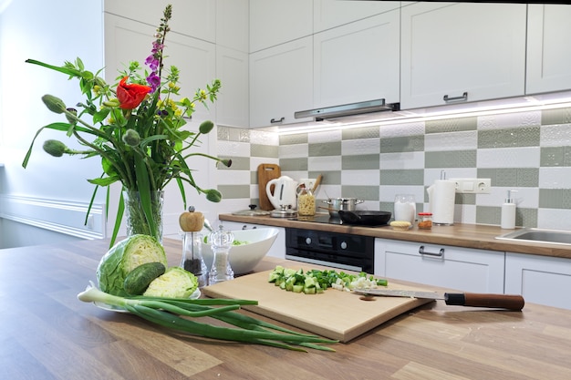 Kochen zu Hause, Gemüse für Salat Kohlgurke Frühlingszwiebeln auf Schneidebrett mit Messer, Hintergrund Küchenmöbel Interieur, Zubereitung von Speisen auf Herd, Blumenstrauß