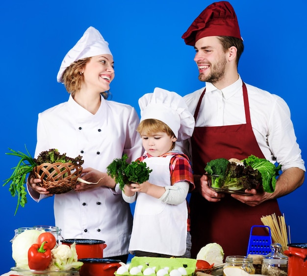 Kochende glückliche familie, die zusammen das abendessen in der küche zubereitet, eltern, die dem kleinen sohn beibringen, wie man kocht