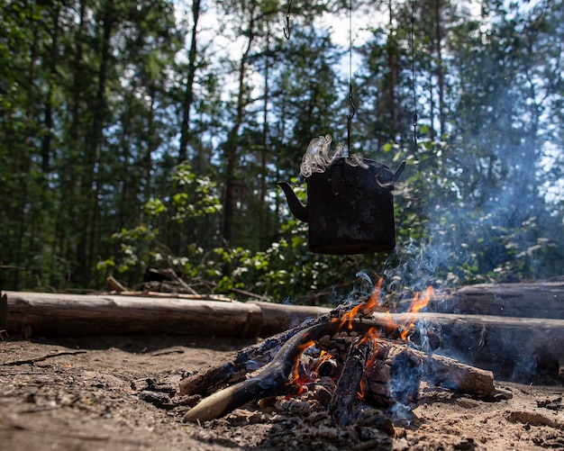 Kochender Rußkessel mit heißem Getränk, das an Haken über dem Lagerfeuer in einem Wald hängt