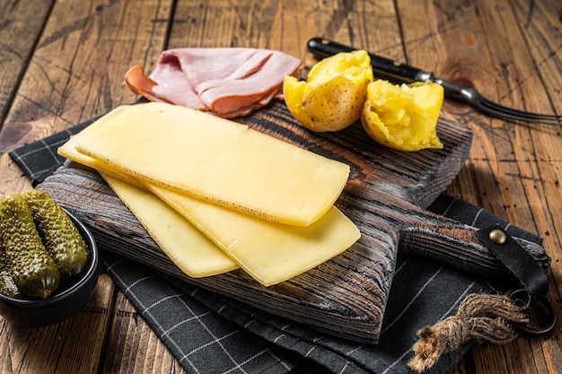 Foto kochfertig raclette schweizer käsescheiben mit salzkartoffel und schinken. hölzerner hintergrund. ansicht von oben.