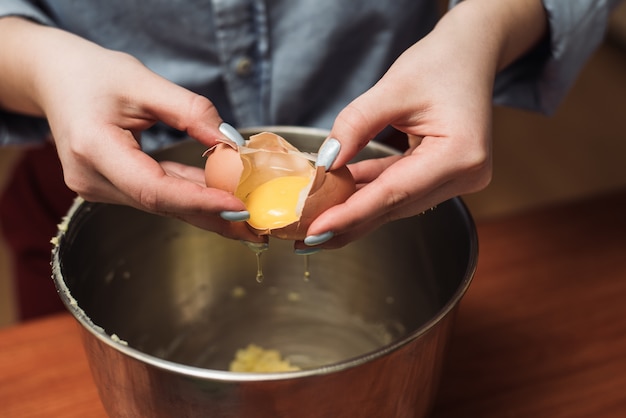 Kochfrau bricht Eier in einer Schüssel für Teig. Eigelb zum Kochen hinzufügen. Der Mann bricht das Ei in eine Metallschale