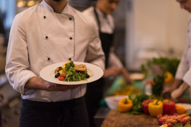 Kochhände halten gebratenes Lachsfischfilet mit Gemüse zum Abendessen in einer Restaurantküche