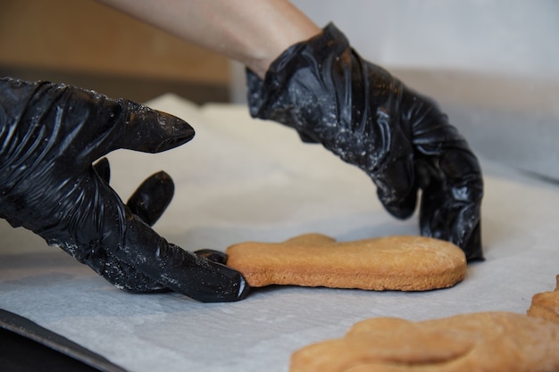 Kochhände in Handschuhen in der Küche bereiten Kekse vor