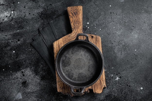 Kochhintergrund mit leerer gusseiserner Pfanne auf rustikalem Handtuch Schwarzer Hintergrund Draufsicht Kopierbereich