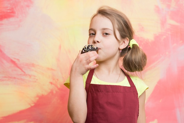 Kochkind mit kleinem Kuchen. Kleines Mädchen auf buntem Hintergrund. Kindheit und Bildung. Kind in Kochschürze. Kochen und Essen.