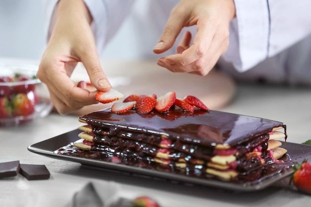 Kochkonzept Professioneller Süßwarenhersteller, der köstlichen Kuchen mit Erdbeer-Closeup schmückt