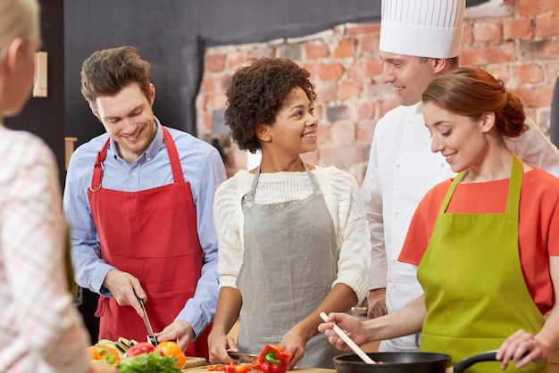 Foto kochkurs, kulinarisch, essen und personenkonzept - glückliche gruppe von freunden mit männlichem koch, der in der küche kocht und spricht