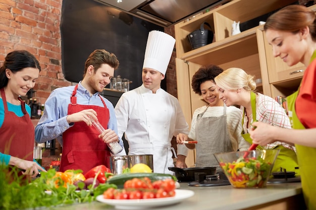 Foto kochkurs, kulinarisch, essen und personenkonzept - glückliche gruppe von freunden und männlicher koch kochen in der küche