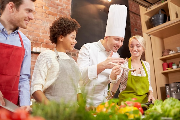 kochkurs, kulinarisch, essen und personenkonzept - glückliche gruppe von freunden und männlicher koch kochen in der küche