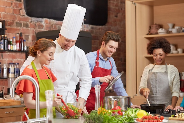 kochkurs, kulinarisch, essen und personenkonzept - glückliche gruppe von freunden und männlicher koch kochen in der küche