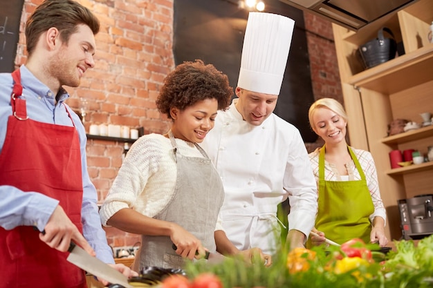 kochkurs, kulinarisch, essen und personenkonzept - glückliche gruppe von freunden und männlicher koch kochen in der küche