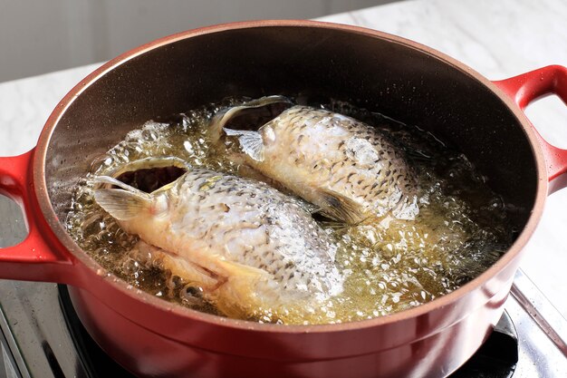 Kochprozess zu Hause, Nahaufnahme von Braten von Fisch mit viel Öl mit roter Pfanne.