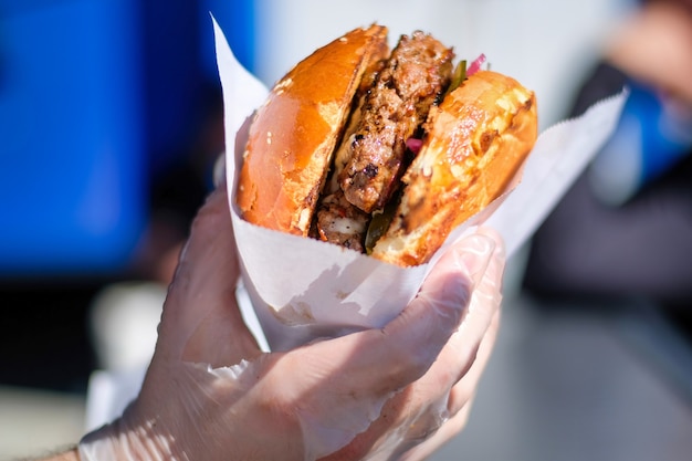 Foto kocht die hand, die den fertigen burger in einer papierhülle hält, bbq