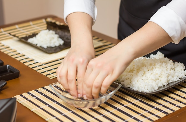 Köchin benetzt die Finger, um Sushi-Rollen zu schließen