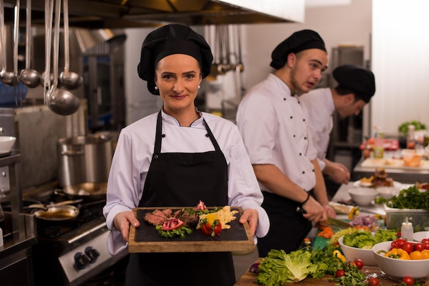 Köchin in Hotel- oder Restaurantküche mit gegrillter Rindersteakplatte mit Gemüsedekoration